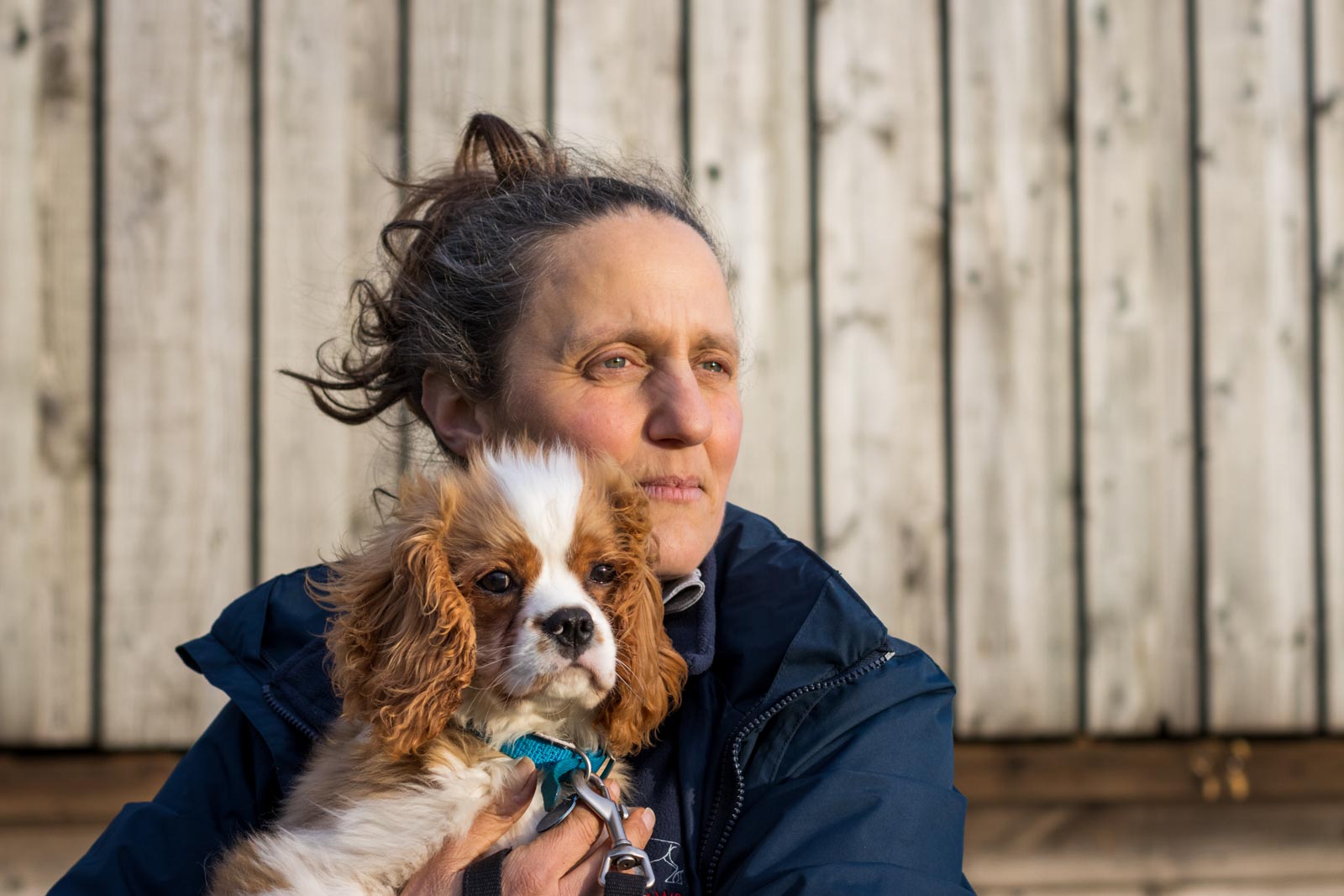 Frau mit Hundewelpe im Arm vor Holzgebäude