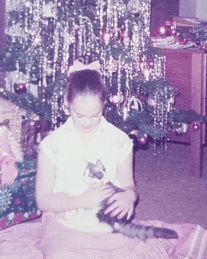 Mädchen sitzt auf dem Boden vor einem Weihnachtsbaum und hält ein getigertes Kätzchen im Arm