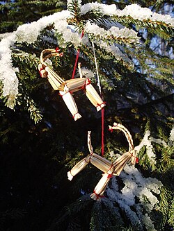 Strohfiguren des Julbocks hängen an einer schneebedeckten Tanne