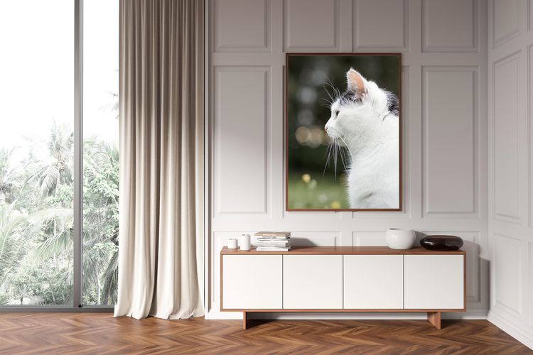 Helles Wohnzimmer mit Sideboard und großem Fenster. Über dem Sideboard hängt ein großes Wandbild mit dem Portrait einer Katze