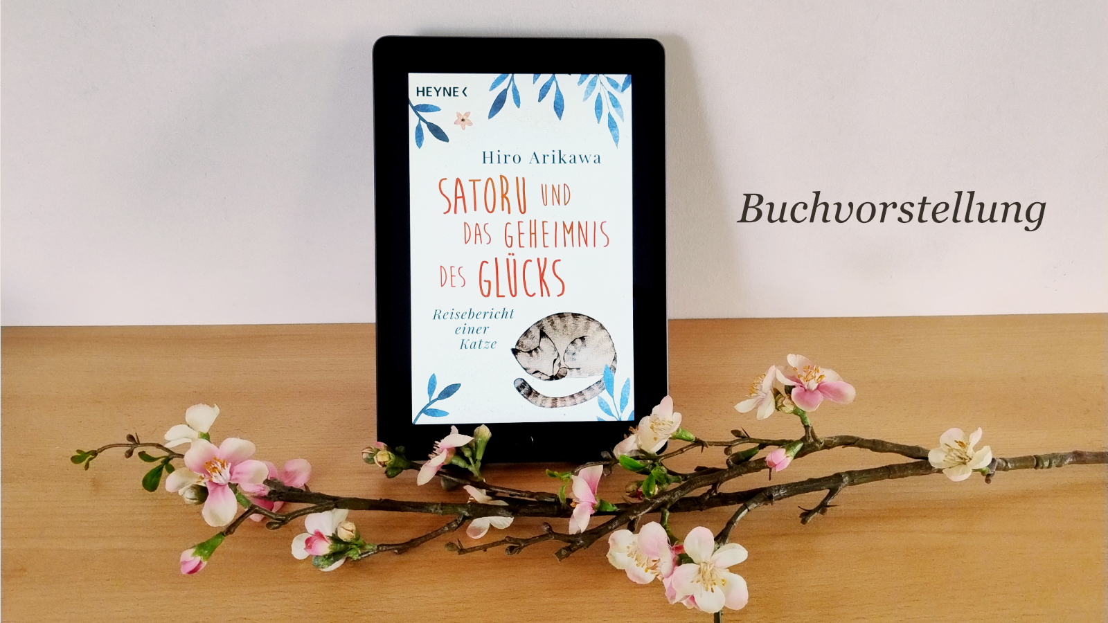 Deko-Kirschzweig liegt vor iPad mit geöffnetem eBook "Satoru und das Geheimnis des Glücks". Text = "Buchvorstellung"