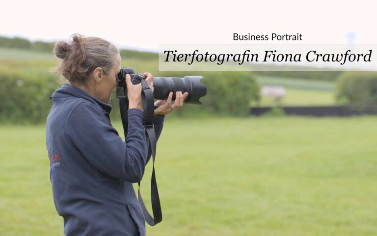 seitliches Portrait einer Frau mit Kamera auf offenem Gelände. Text = "Business Portrait - Tierfotografin Fiona Crawford"